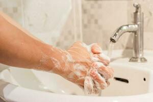 de cerca de masculino Lavado manos frotamiento con jabón terminado lavabo en baño a hogar. higiene concepto foto