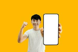 Asian Man Holding Smartphone With White Empty Screen On Yellow Background. Cellphone display Mockup for Mobile App Advertisement. photo