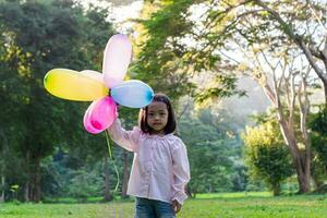 Portrait of child girl holding colorful toy balloons in the park outdoors. photo