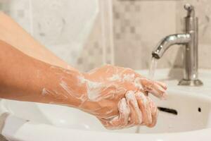 Close-up of male washing hands rubbing with soap over sink in bathroom at home. Hygiene concept photo