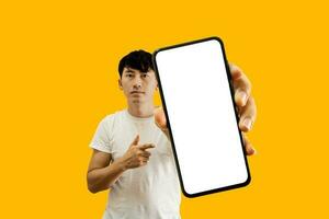 Asian Man Holding Smartphone With White Empty Screen On Yellow Background. Cellphone display Mockup for Mobile App Advertisement. photo