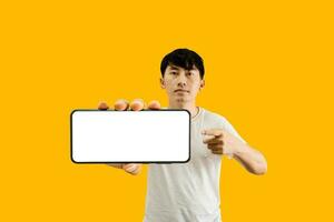 Asian Man Holding Smartphone With White Empty Screen On Yellow Background. Cellphone display Mockup for Mobile App Advertisement. photo