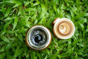 Black coffee in a thermos on the green grass,  selective focus, and soft focus. photo