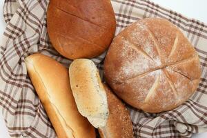 recién horneado un pan pan bollo rodar redondo largo mezcla verdad envuelto en a cuadros cocina tela servilleta toalla terminado blanco antecedentes foto