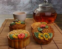 Colorful flower decorated mooncake cut slice half layer Chinese mid autumn festival on bamboo food mat glass teapot white ceramic teacup photo