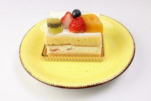 Kiwi strawberry blueberry mango fruit cream layer cake on rustic yellow plate over white background photo