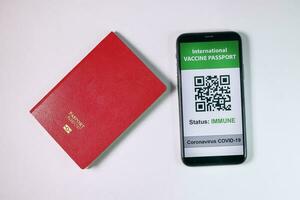Digital international vaccine passport smart phone screen qr code app coronavirus covid 19 immunization red passport book on white background photo