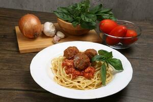 Cooked spaghetti sauce meat ball cheese powder on white plate with ingredients roma tomato glass bowl basil onion garlic wooden board recipe on table marble wall photo
