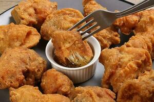 Light battered deep fried chicken variety mix pieces pile flaky meat on grey plate on fork dripping honey garlic clear sauce in center over wooden background photo