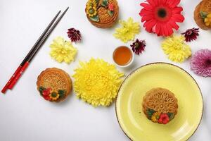 Colorful flower decorated moon cake Chinese mid autumn festival tea in small white teacup chopsticks plates bowl blue yellow violet chrysanthemum mum red daisy flower on white background photo