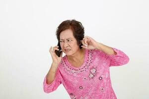 Elderly asian Chinese female on white background talking on phone can not hear face expression finger in other ear photo