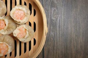 Prawn shrimp shaomai dim sum dumpling in bamboo steamer on rustic wood background photo