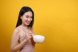 Beautiful young south east Asian woman holding chines empty chopstick Chinese soup spoon bowl utensil pretend acting posing see eat taste smell feed offer satisfaction yummy yellow orange background photo