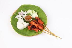 Chicken beef mutton meet Satay set nasi impit sticky rice cake sliced onion cucumber sweet peanut sauce on banana leaf bamboo basket on white background photo