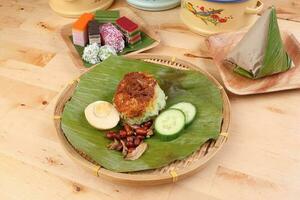 Nasi Lemak fragrant rice coconut milk with sambal friend peanut anchovy egg packed banana leaf round bamboo plate colorful nyonya kuih sweet desert palm leaf plate on wooden background photo