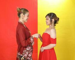 Two Asian woman traditional kebaya and modern dress red yellow paper background meet great photo