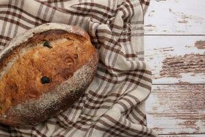 Rustic whole grain artisan bread loaf with cranberry raisin dry fruit nuts wrapped in checkers cloth with wooden table top flat lay view photo