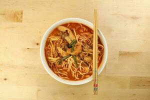 Malaysian curry yellow mee noodle with roasted chicken slice in white bowl chopstick on wooden background photo