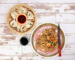 Home style dim sum dumpling in bamboo steamer chili flake oil sauce Stair fried noodle with prawn seafood tofu colorful pepper on oriental style plate chopsticks over rustic wooden background photo