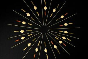 dry raw spaghetti conchiglie seashells fusilli cork screw color pasta laid on black background sunray glow pattern concept photo