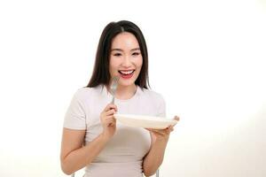 Beautiful young south east Asian woman holding white empty white plate fork spoon on other hand eat taste look see food photo