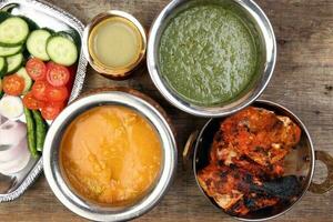 Spicy red Chicken grilled tikka tandoori nan bread green spinach curry yogurt sauce dal tomato cucumber onion salad set in metal stainless steel brass copper pot on rustic vintage wood background photo