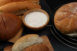 Freshly baked bread loaf bun roll round long mix verity flour in wooden bowl on wooden board metal grill over black background photo