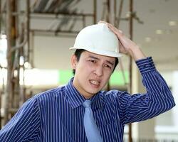 South East Asian young Malay Chinese man wearing white yellow safety helmet tie hand on head worried tensed photo