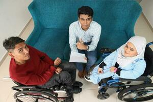 Portrait of young man and woman talking discussing work business. Two on wheelchair are paralyzed and one sitting on sofa adhd also Autism autistic photo