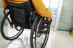 Young man south east Asian malay sitting on wheelchair look outside over balcony window . Paralyzed due to accident. Close up of hand and wheel photo