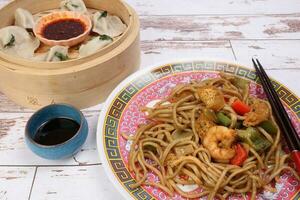 Home style dim sum dumpling in bamboo steamer chili flake oil sauce Stair fried noodle with prawn seafood tofu colorful pepper on oriental style plate chopsticks over rustic wooden background photo