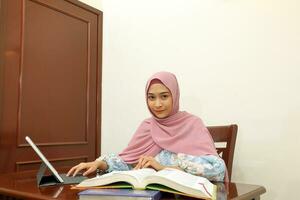 young Asian Malay muslim woman wearing headscarf at home office student sit at table computer book file paper study work photo