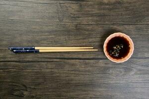 Bamboo wooden chopsticks and chili soya sauce in small ceramic bowl dish on rustic wood background photo