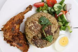 Beef Biryani Tehari with boiled egg coriander leaf garnish chicken curry pot roasted leg tomato cucumber onion chili coriander salad on white plate set over white background photo