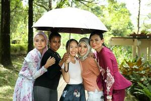 group of woman friends Malay Chinese Indian Asian outdoor park lake nature walking under one umbrella secure safe rain photo