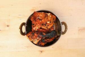 Spicy red Chicken grilled tikka tandoori in metal brass copper pot on light wood background photo