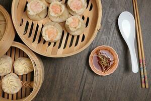 Prawn shrimp shaomai Xiao long bao dim sum dumpling chicken prawn fish seafood vegetable in bamboo steamer sauce chopsticks on rustic background photo