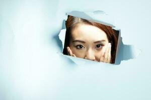 Young beautiful Asian woman expression through torn paper hole photo