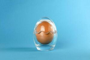 Egg in egg shape glass container protection shell on blue background safety security photo