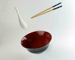Empty oriental Japanese Chinese soup bowl spoon chopstick elevated flying in air red black white photo