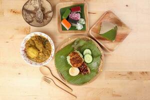 Nasi Lemak fragrant rice coconut milk with sambal friend peanut anchovy egg packed banana leaf round bamboo plate colorful nyonya kuih sweet desert palm leaf plate on wooden background photo