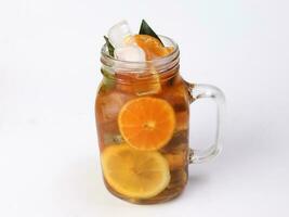 Liquid ice lemon orange tea with slice green leaf cinnamon stick in transparent glass jar mug on white background photo