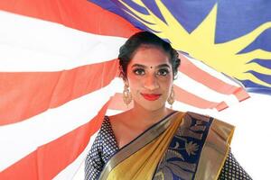 South east Asian Indian race ethnic origin woman wearing Indian dress costume sharee multiracial community holding under Malaysian flag Jalur Gemilang on white background photo