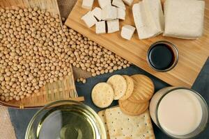 Soyabeans products soya beans flowing bamboo sieve wooden board on jute black stone slate background curd tofu oil milk sauce biscuit cookies photo