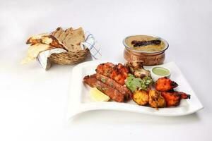 Mixed grill kebab chicken mutton beef prawn fish mint sauce lemon pickled onion bread basket chapati naan tandoori paratha dal lentil fry tadka copper pot on white dish over white background photo