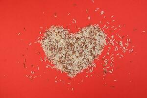 Mixed low glycaemic index healthy rice grain basmati millet buckwheat red rice hart shape on red background photo