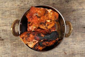 Spicy red Chicken grilled tikka tandoori in metal brass copper pot on rustic vintage wood background photo