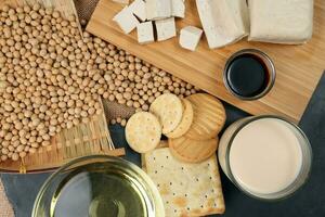 Soyabeans products soya beans flowing bamboo sieve wooden board on jute black stone slate background curd tofu oil milk sauce biscuit cookies photo