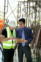 South East Asian young Malay Chinese man wearing white yellow safety helmet vest tie study see talk clipboard outdoor construction site photo