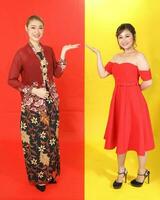 Two Asian woman traditional kebaya and modern dress red yellow paper background hands palm showing display photo